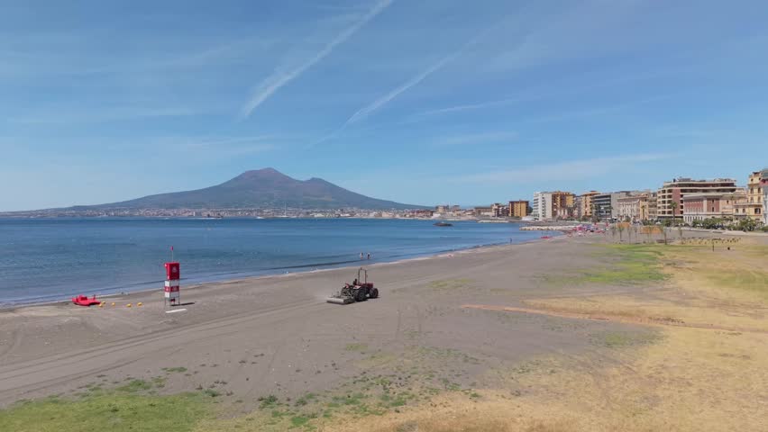 Aerial view of Mount Vesuvius overlooking beach maintenance tractor on the waterfront of Castellammare di Stabia, Gulf of Naples, Italy