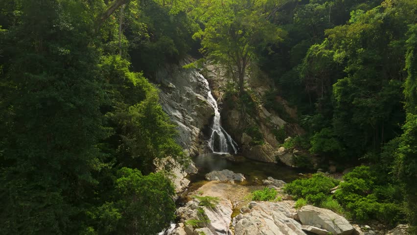 Slow aerial approach to tall Quebrada Valencia waterfall cascading down rocky cliff into pool surrounded by lush green jungle near Santa Marta Colombia