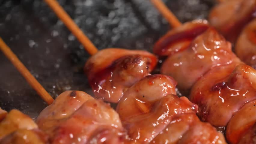close-up of traditional Japanese yakitori chicken skewers. The footage highlights the glistening, dark amber teriyaki glaze dripping over succulent, grilled meat on bamboo skewers, capturing the steam