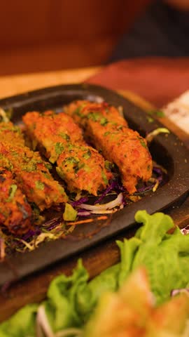 Close-up of hand using fork to lift spiced meat kebab from hot sizzler plate.