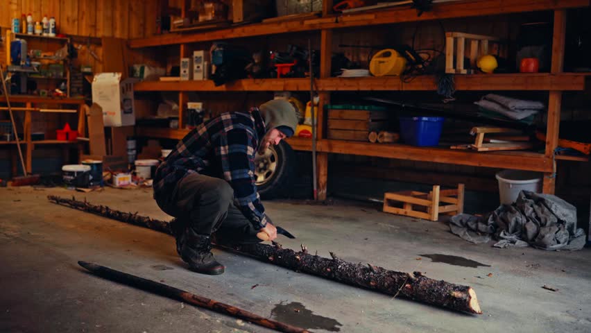 A Man With An Axe Removing Tree Bark Inside A Garage Shop. Static Shot