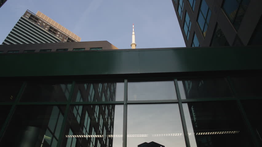 CN Tower revealed between modern glass office buildings. Tracking backward shot.