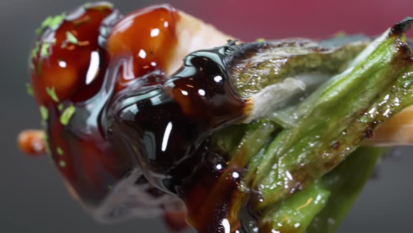 An extreme macro slow motion shot of traditional Japanese Negima yakitori featuring grilled chicken thigh meat and green scallions covered in a glossy, dripping brown teriyaki tare sauce.
