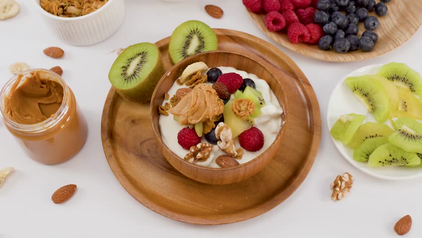 Overhead view of hands arranging a nutritious yogurt bowl with berries, kiwi, and granola.