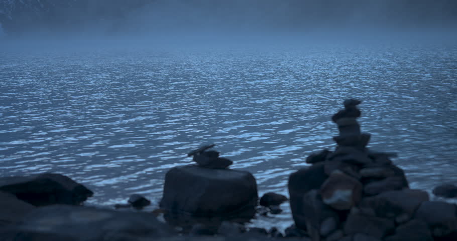 Gokyo Lake. Everest Region, Nepal, static shot of traditional stone cairns stacked along the lakeshore with low mist drifting over the water surface.
