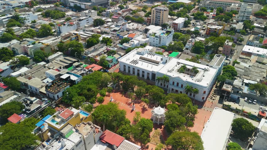 Aerial descent towards Parque de Los Novios with white gazebo Manuel Murillo Toro monument and red brick plaza framed by green trees in historic Santa Marta Colombia