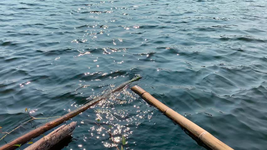 Closeup of bamboo poles floating on the rippling blue water of a lake on a sunny day