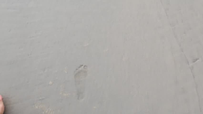 Close-up photograph of a sandy surface resembling a beach or shoreline, highlighting fine grain textures, natural patterns, and organic details formed by the environment.
