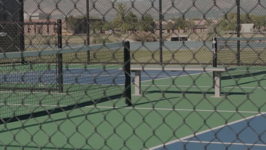 Slow motion left to right pan across empty pickleball courts behind chain link fencing.