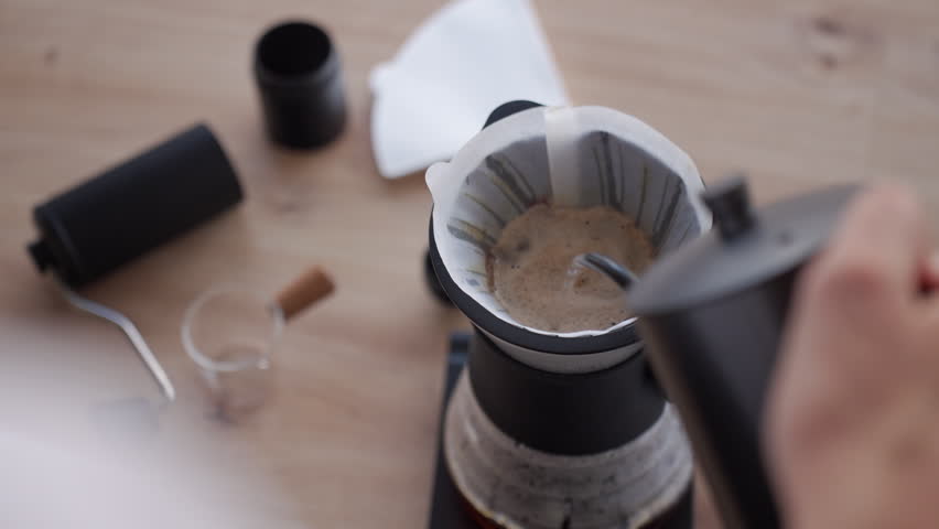 Process of brewing drip coffee at home. Hot water pours over coffee grounds in a paper filter, creating bloom in a coffee dripper