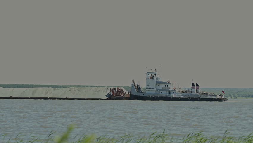White tugboat pushing large loaded barge along wide calm river
