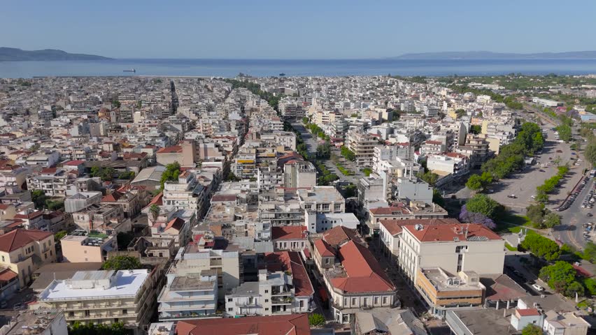 Drone footage over Kalamata city center in southern Greece, featuring a wide panoramic view of the urban landscape, long straight streets, compact residential and commercial buildings, red tiled rooftops and the blue waters of the Messinian Gulf in the background. The clip highlights the structure of the city, coastal setting and everyday Mediterranean atmosphere from above.