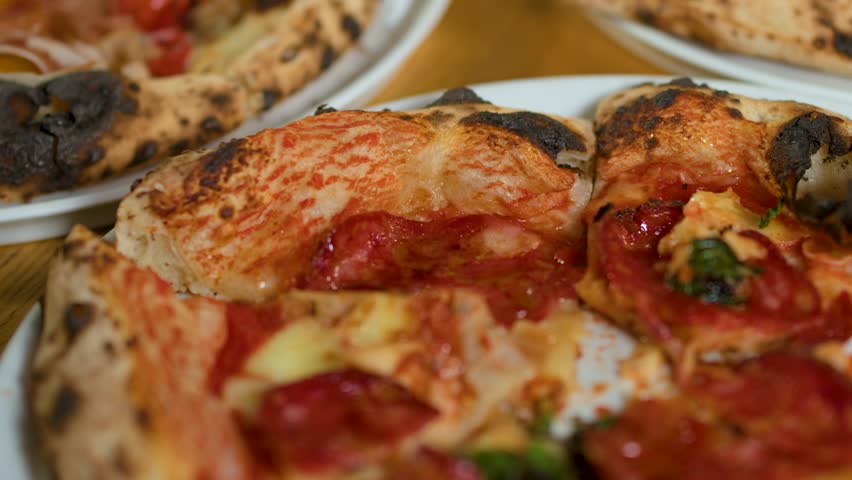 Close-up panning shot of artisanal wood-fired pizzas with pepperoni and sourdough crust on restaurant tables.