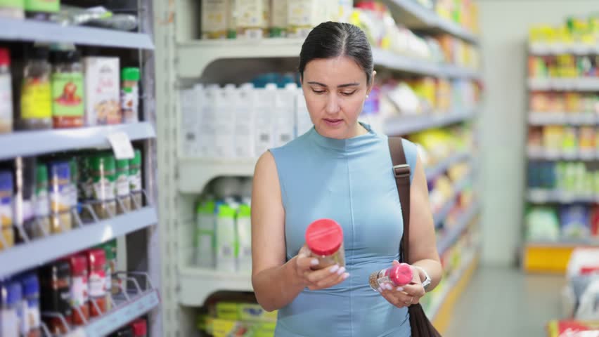 In supermarket woman choose dried spices, examines packages of food. Attentive customer meticulously studies goods in self-service store. Client interested and figure out list of ingredients