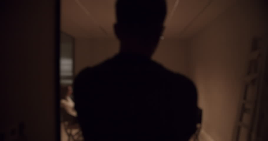 Ominous shot of a man walking down a dimly lit hallway towards a secret meeting in progress, creating a suspenseful and clandestine atmosphere perfect for thriller or espionage concepts