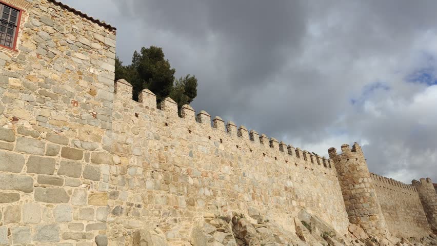 Majestic stone wall of the historic city of avila, a unesco world heritage site in spain, featuring an impressive arch and gallery under a cloudy sky on a sunny day in castile and leon
