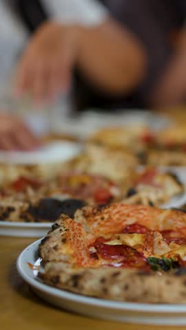 Close-up shot of people sharing fresh Neapolitan pizza on a wooden table in warm lighting.
