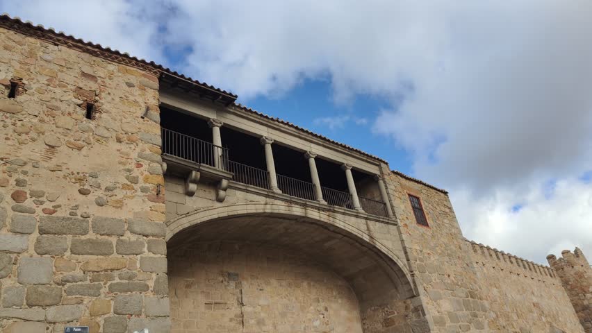 Low-angle perspective revealing the historic fortified walls of avila, spain, showcasing the medieval architecture of the palace of los davila with its prominent stone arch and balcony