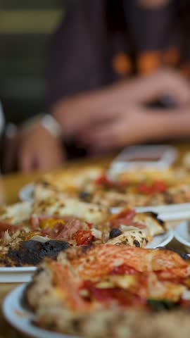 A hand lifts a fresh margherita pizza slice from a table in a restaurant.