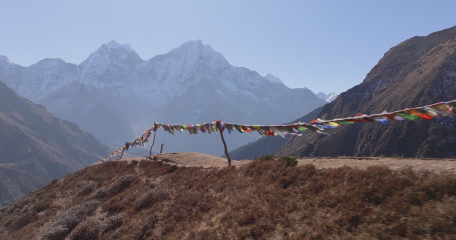 Everest region Nepal, aerial gliding shot of colorful Buddhist prayer flags fluttering on a ridge with Mount Thamserku and snow capped Himalayan peaks behind.