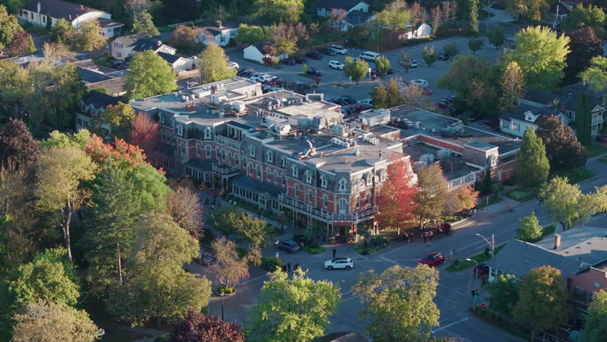 A close-up drone orbit around the historic Prince of Wales Hotel in Niagara-on-the-Lake, Ontario, surrounded by vibrant autumn trees on a sunny afternoon.