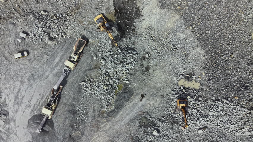 Heavy machines work to extract granite from a quarry while trucks transport materials in a busy rocky area during the day