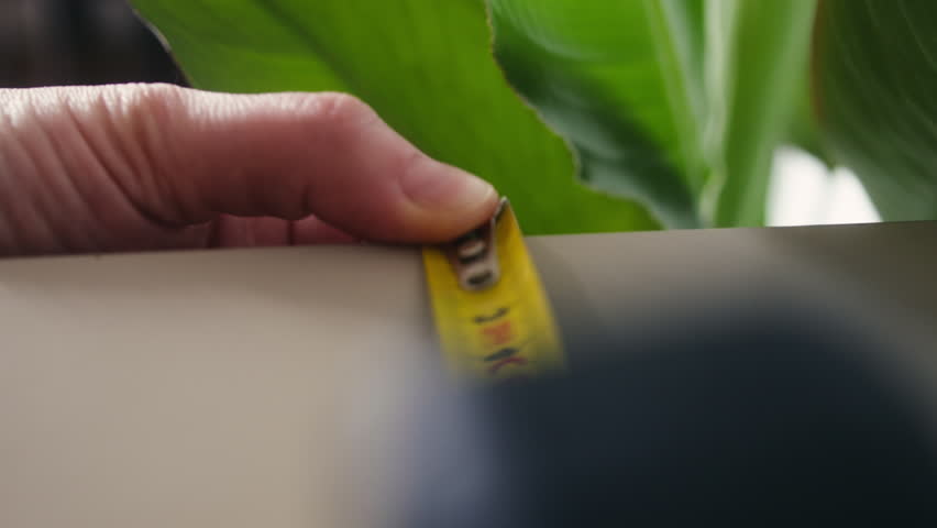 Close-up tracking shot following a measuring tape while taking measurements of furniture. Home improvement, interior design and DIY project concept. High quality 4k footage