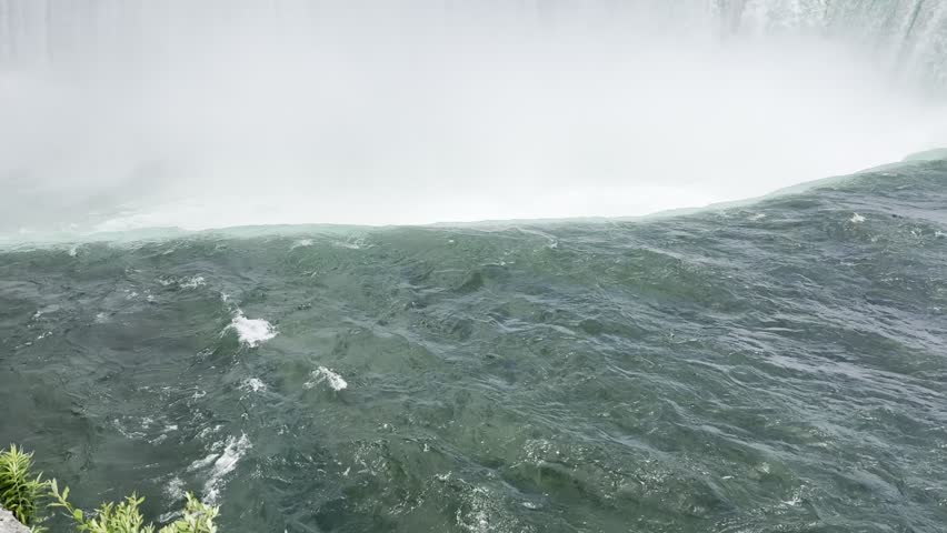 Beautiful view on the Niagara Falls and the Niagara River. Canada. Water flows rapidly over rocks at a waterfall, creating mist and ripples on the surface, surrounded by lush greenery and rocky terrain