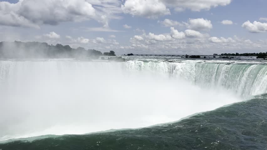 Beautiful view on the Niagara Falls and the Niagara River. Canada. Niagara Falls displays powerful cascading water with mist rising, surrounded by lush greenery and a bright blue sky filled with clouds