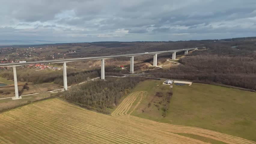 In Somogy County, the Kőröshegyi Völgyhíd spans the rural landscape as a long concrete viaduct on the M7 highway, crossing fields near Lake Balaton under a cloudy winter sky in a bird