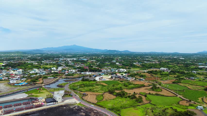Aerial view of Singyemul Park in Sinchang-ri Hangyeong-myeon Jeju Island revealing coastal village black lava rocks rice paddies and Hallasan mountain