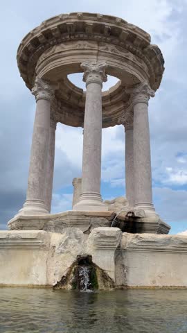 The majestic columns of the historic monumental fountain at the Ancient City of Kibyra and the serene scene of its clear, flowing water beneath a mesmerizing cloudy sky.