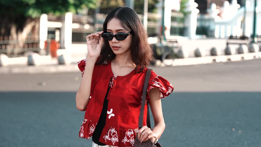 Pretty young Asian woman wearing Indonesian traditional batik shirt is standing and posing in the downtown.
