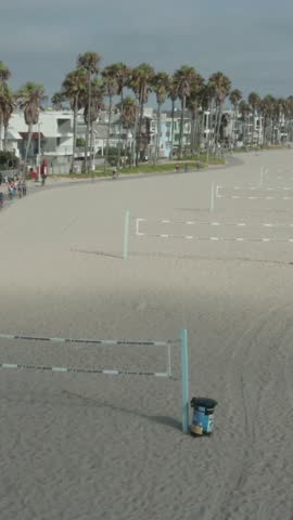 AERIAL: Flight over beach with volleyball nets at Venice Beach with palm trees and bike lane, Sunny, Los Angeles California 