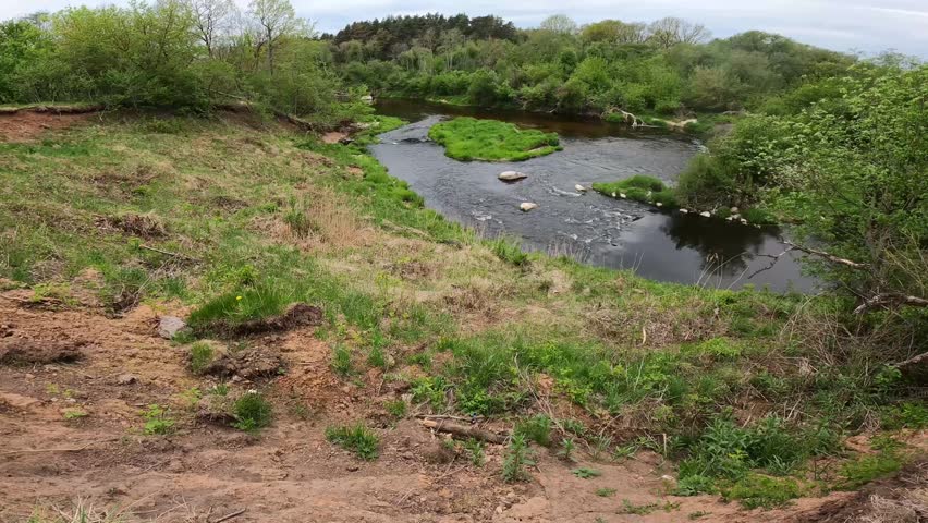 View of riverbank soil erosion and cliff collapse with an old campfire site on a steep river shore