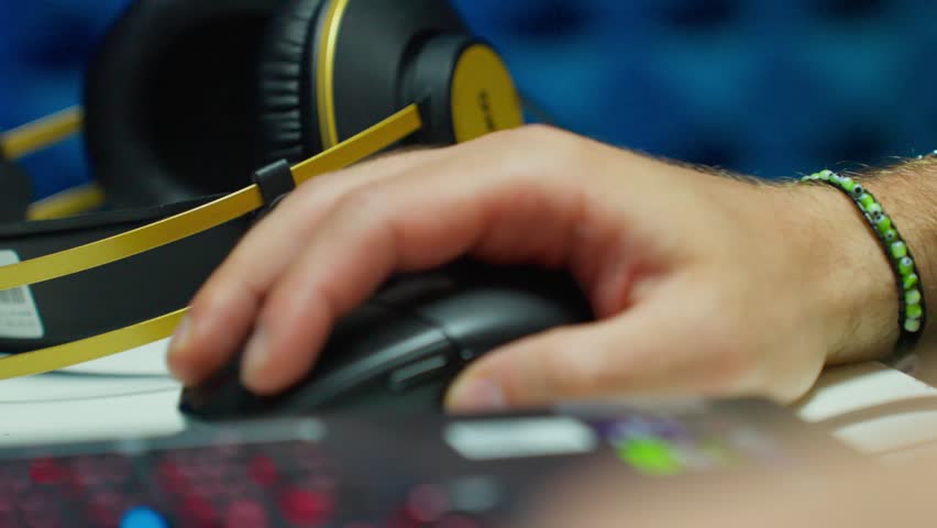 Gamer hand controlling mouse over RGB keyboard with headphones in background at late sequence