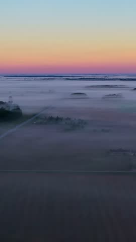 Aerial view of a foggy countryside landscape at sunrise with vibrant sky colors.