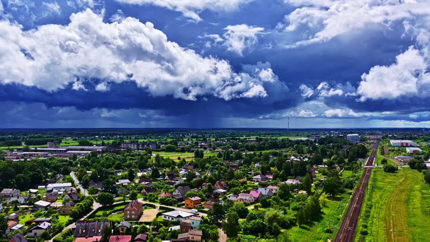 Impressive dark storm clouds forming over a small european town with green trees and a railway