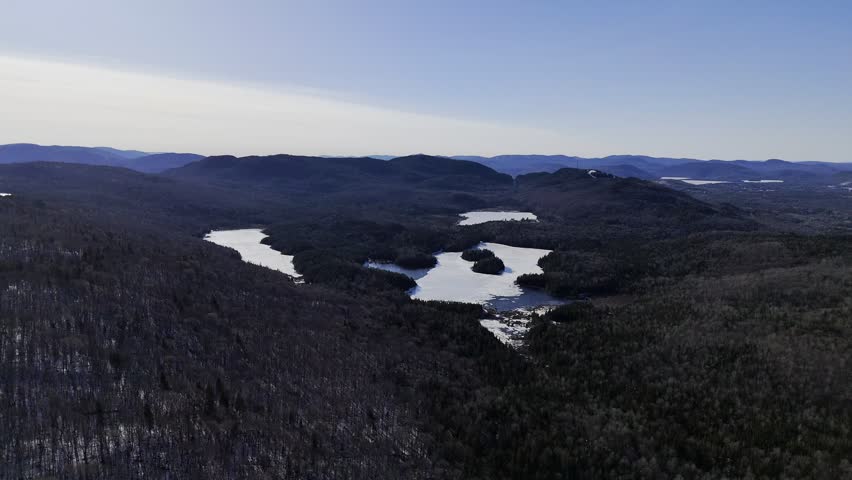 defaultAerial view of winding road along frozen lake in Quebec with forest and mountains under blue sky. g.