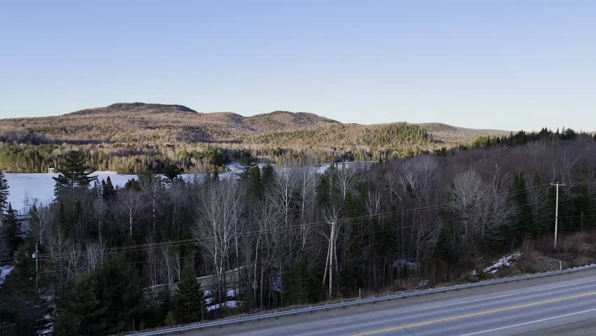 defaultAerial view of winding road along frozen lake in Quebec with forest and mountains under blue sky. g.