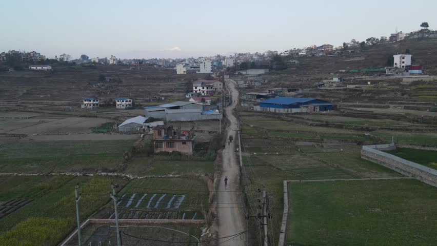 Aerial Drone View of Urban Expansion and Green Farmlands Beneath a Mountain Range in Nepal