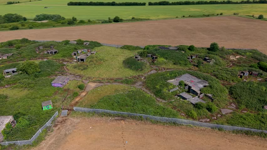 ZE1 gun emplacements, Chadwell Heath aerial orbit showing WWII anti-aircraft battery concrete bunkers, magazine huts and access paths amid overgrown grassland on former RAF London defences site.