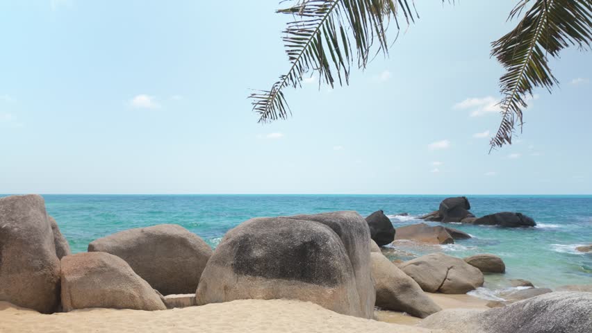 Large granite boulders and palm leaves frame a tranquil tropical beach shoreline
