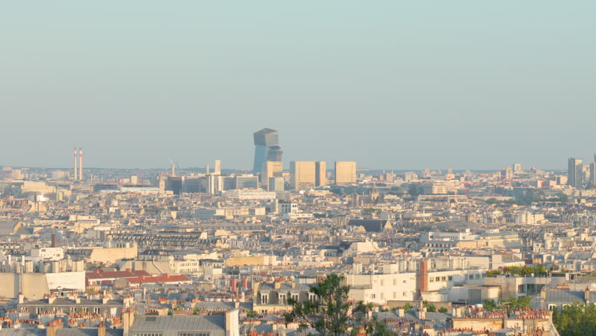 A wide scenic panorama capturing the expansive cityscape of Paris, showcasing layers of urban architecture and distant skyscrapers under a clear bright sky.