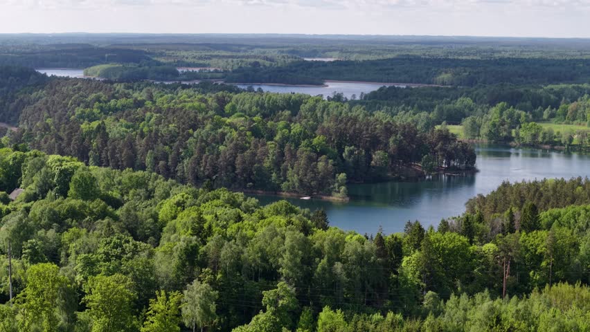 Drone panning over forest-surrounded lake and rural Lithuanian countryside