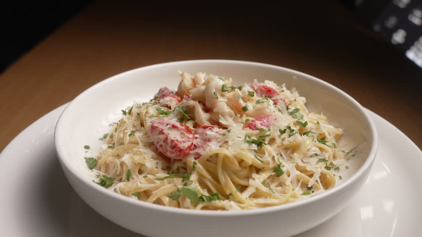 Creamy shrimp pasta with fresh parsley and grated parmesan cheese rotating on a serving plate, fa01