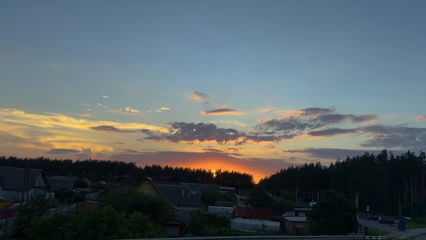 Golden sunset over rural village and pine forest, spectacular evening cloudscape in the background.