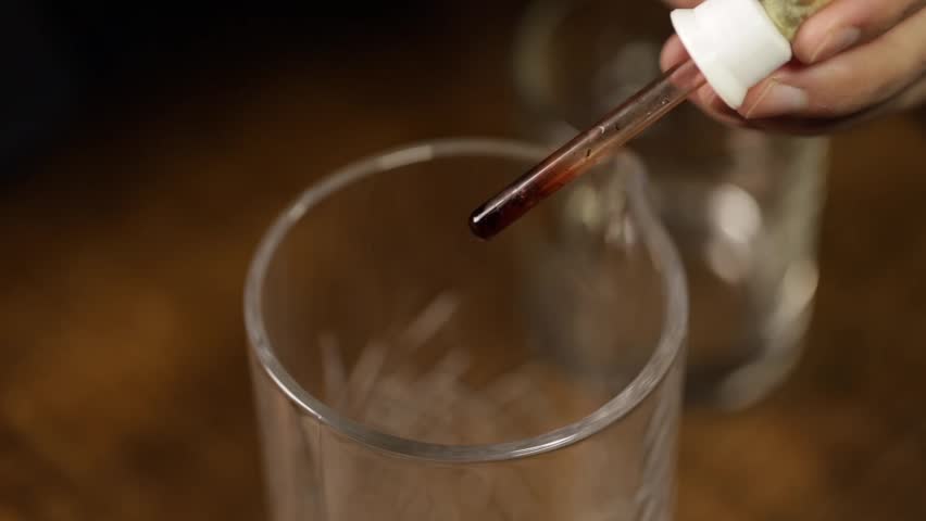 bartender pouring drops of orange bitter into a mixing glass. Bartender preparing an old-fashioned refreshment.