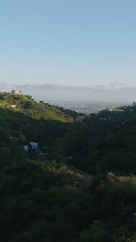 Forwards fly above hilly landscape with residences on city outskirts at golden hour. Los Angeles, California, USA
