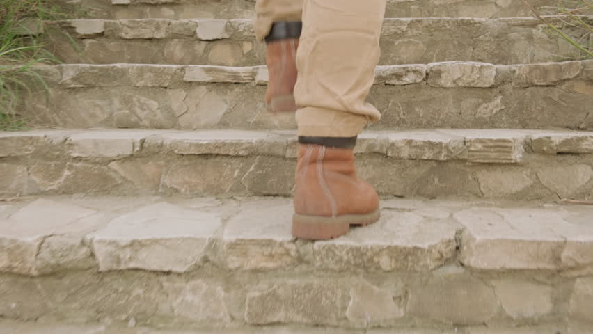 Feet in boots climb up stone steps of stairs outdoors close-up.